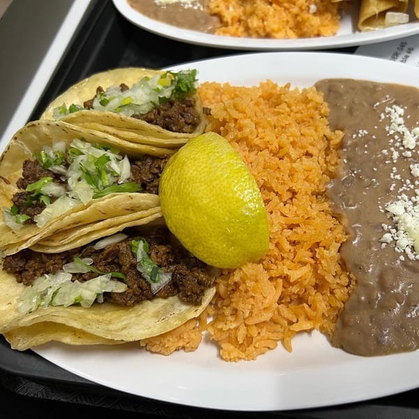 Three MLT tacos with meat, onions, and cilantro, served with rice, refried beans, and a lime.