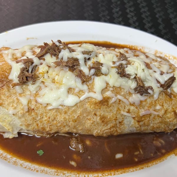 A large, cheesy burrito with shredded beef and red sauce on a white plate at Mi Linda Tierra Taqueria.
