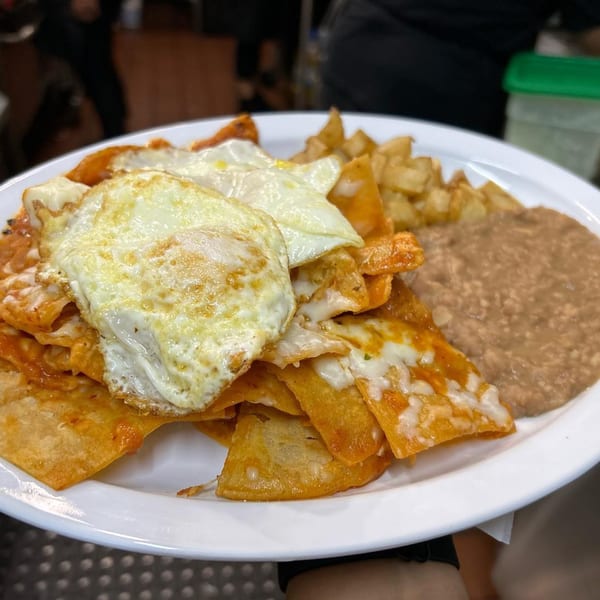 MLT chilaquiles with fried eggs, potatoes, and refried beans on a white plate.