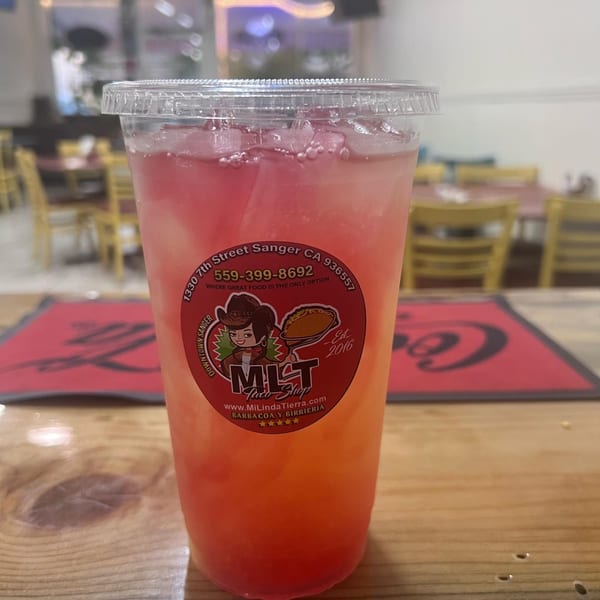 A vibrant pink and orange drink with ice in a clear cup with the MLT Taqueria logo.