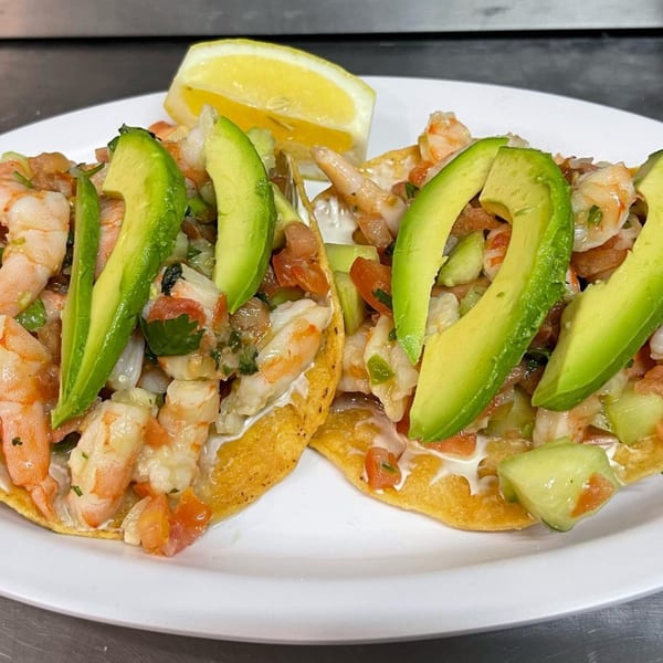 Two shrimp tostadas with avocado slices, pico de gallo, and a lemon wedge on a white plate.
